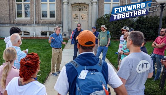 A group of people gather around a person directing a tour on the Duke University campus