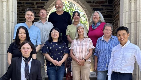 Eleven people pose on a short flight of steps leading to a gothic arch.