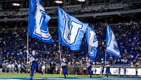 Duke cheerleaders carry flags onto the field.