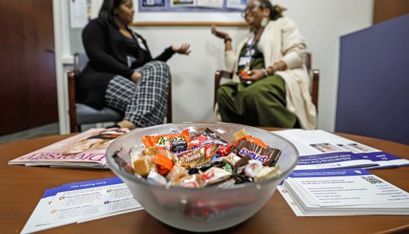 A candy bowl sits on a table as two people talk in the background