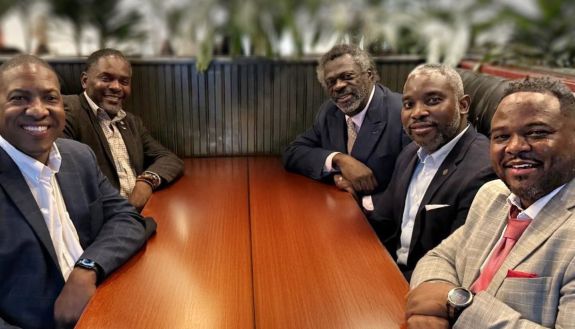 Six men sitting at a table looking at the camera