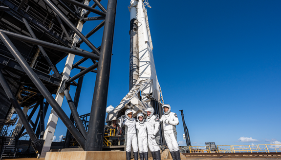 civilians in front of a space ship dressed in flight suits