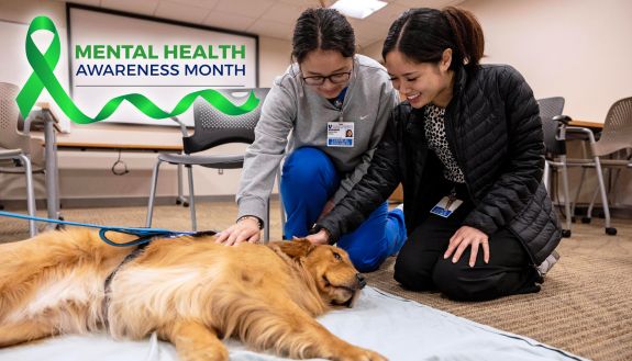Two women kneel next to a sleeping golden retriever to pet it.