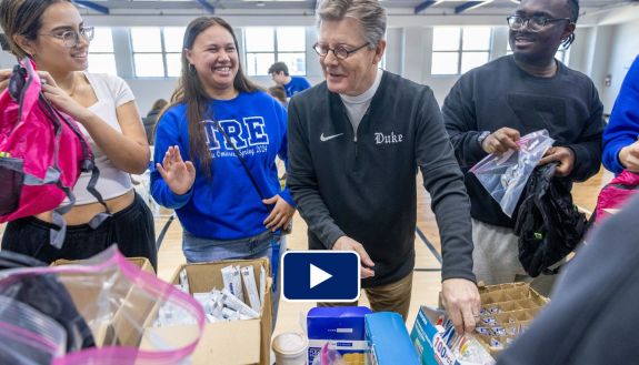 A group of people assembling items to put in backpacks, with Duke President Vincent Price in the middle