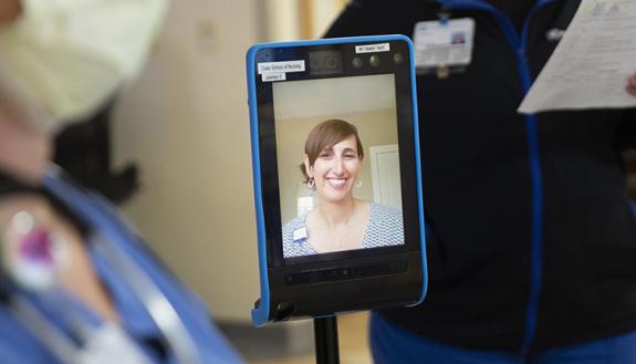 Technology connects health care worker working remotely to a patient in hospital bed.