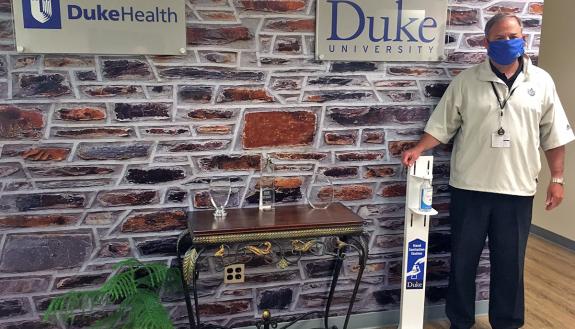 Adam Barnes stands next to a hand sanitizer dispenser.