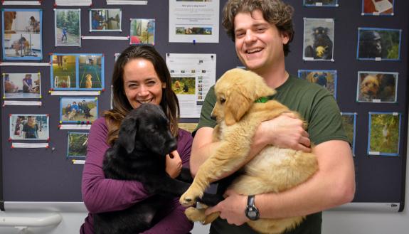 Vanessa Woods, left, holds Ernie while Brian Hare carries Kyler. The two puppies are being trained to become assistance dogs.