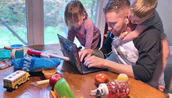 Kyle Fox working at his laptop with his children.