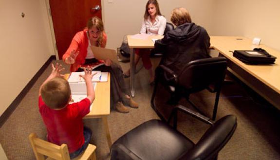 Students Taryn Allen (foreground) and Erin Schoenfelder (white shirt) assess a 5-year-old boy at Duke's Pediatric Psychology Lab. The boys grandmother is seated across from Schoenfelder. Photo by Jon Gardiner/Duke University Photography