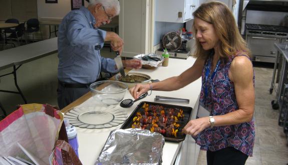 Instructor Sheri Branson (right) and OLLI member Dr. Mike McLeod prepare for a potluck dinner on May 31, the culmination of the “What’s Cooking” class, which met at Watts Street Baptist Church.