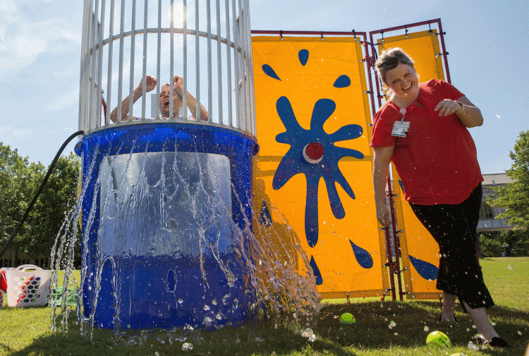 After missing with her throws, Margaret Hardy, MSN, pushes the red button dunking Dr. Dan Blazer during the Dunk-A-Doc fundraising event at Duke Cancer Center on May 16, 2019. Eighteen doctors volunteered to get wet to support cancer research and raise aw