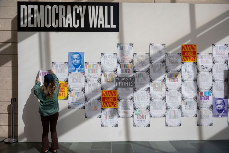 senior Julia Deitelbaum hangs a voting poster on the Democracy Wall at the Nasher.