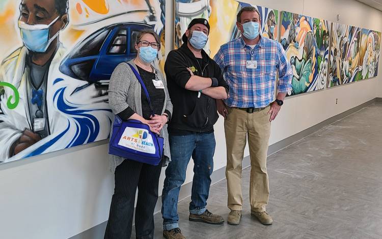 Jennifer Collins-Mancour, visual arts coordinator for Arts and Health at Duke, artist Sean Kernick and Bill Gregory stand in front of the Duke University Hospital mural Kernick that made. 