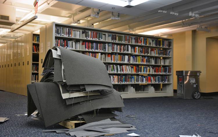 Stacks of old carpet rest next to shelves on Lower Level 2 in Perkins Library. 