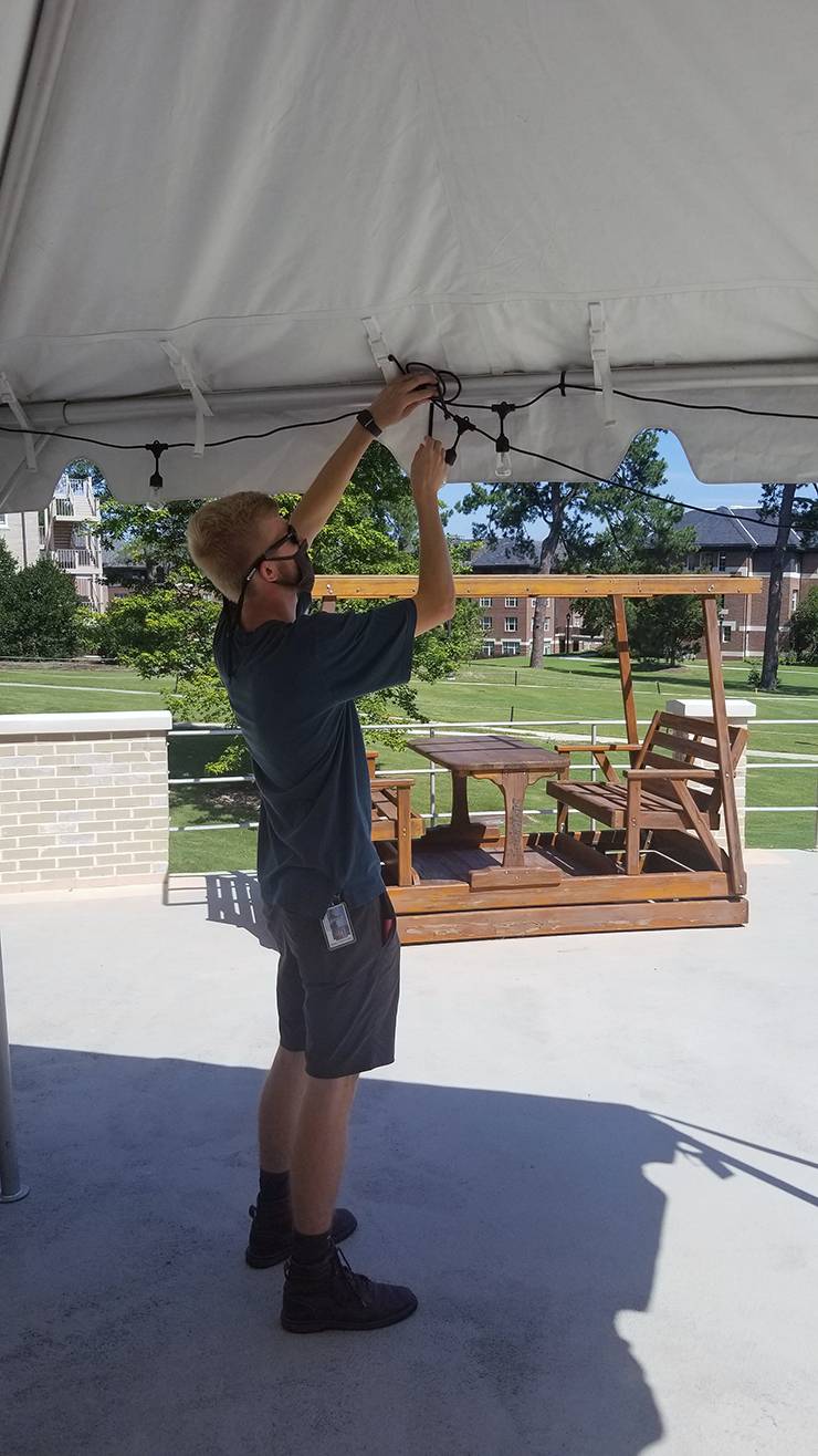 Griffin Matthews of the Venue and Production Management team installs solar-powered lights on one of the tents on East Campus. Photo courtesy of Richard Kless.
