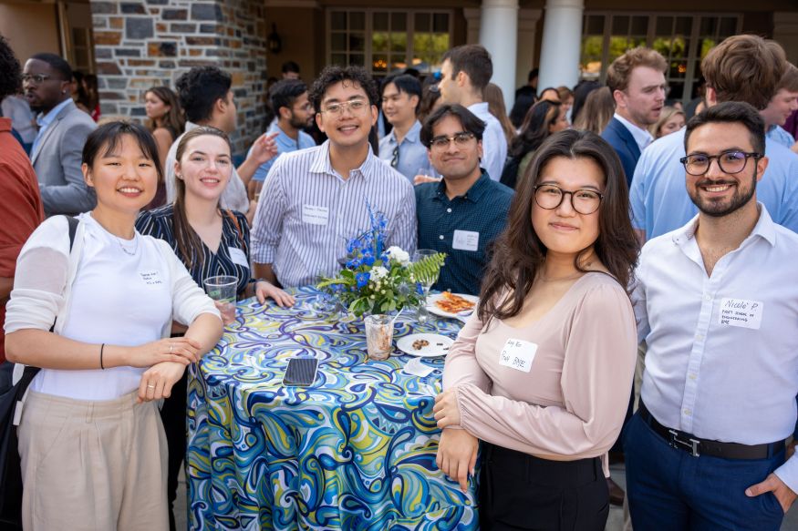 A group of graduate students around a cocktail table pause and pose for a picture