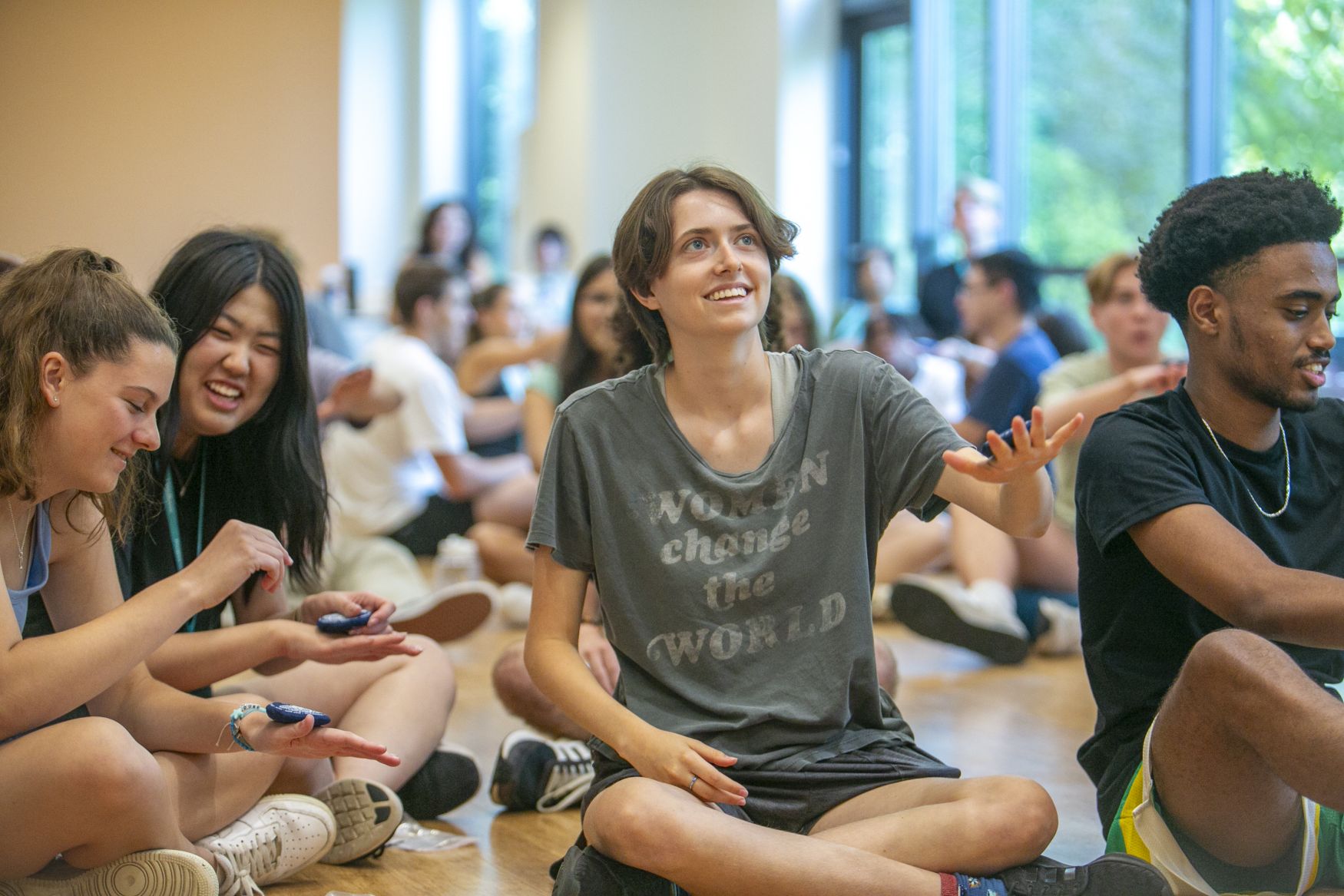 Meehan doing a bean bag exercise holding one hand up with the bag on the back of her hand surrounded by first-years sitting on the floor