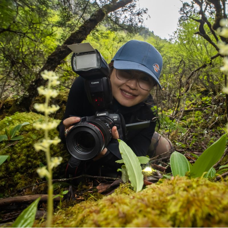 Binbin Li holding a camera crouched in the underbrush