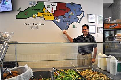 Fares Hanna, the owner of Twinnie's and Blue Express eateries on campus, poses next to a map on the wall that shows the North Carolina food items used in dishes at Blue Express. His eateries received this year's 