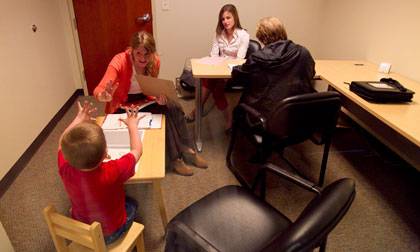 Students Taryn Allen (foreground) and Erin Schoenfelder (white shirt) assess a 5-year-old boy at Duke's Pediatric Psychology Lab. The boys grandmother is seated across from Schoenfelder. Photo by Jon Gardiner/Duke University Photography